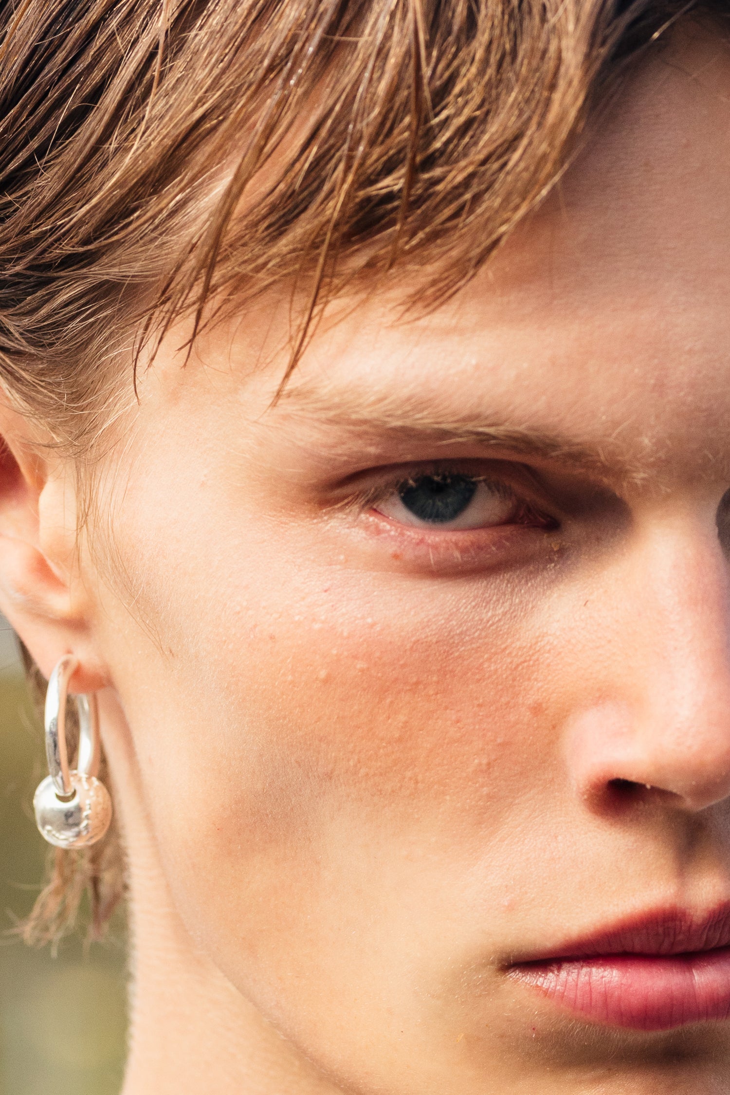 Malli katsoo suoraan kameraan ja hänellä on korvanlehdessään hopeinen Rolf Ekroth x Kalevala Rakas-koru.